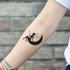 a woman's arm with a tattoo on it that has a silhouette of a fairy sitting on the moon