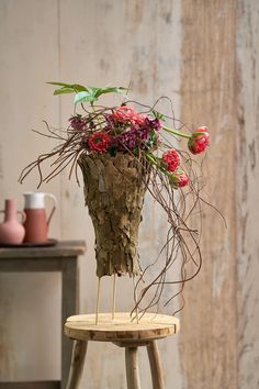 a wooden stool with flowers in it on top of a table next to a wall