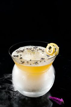 a glass filled with an alcoholic drink on top of a black table next to a purple flower