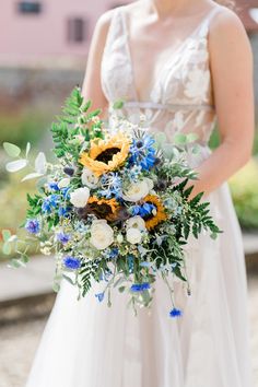 a woman in a wedding dress holding a bridal bouquet with blue and yellow flowers