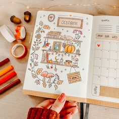 a hand holding an open planner next to other items on a wooden table with markers and pencils