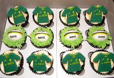 twelve cupcakes with green and white icing in a box, each decorated like a football jersey