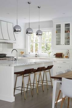 a kitchen with white cabinets and marble counter tops, wooden bar stools in front of an island