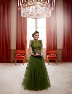 a woman in a green dress standing in front of a chandelier