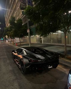 a black sports car is parked on the side of the road at night in an urban setting