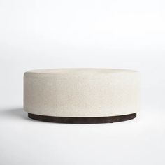 a white round ottoman sitting on top of a white floor next to a black base