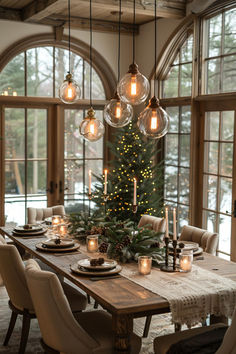 a dining room table with candles and christmas tree in the center surrounded by large windows