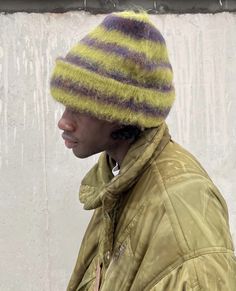 a man wearing a yellow jacket and a striped hat on top of his head while standing in front of a white wall