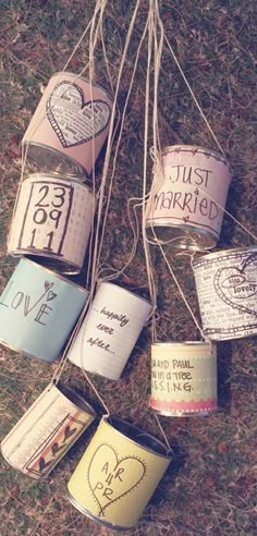 some tin cans are hanging from string on the ground with hearts and words painted on them