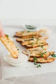 a person dipping something into a small bowl with parsley on the side next to some crackers