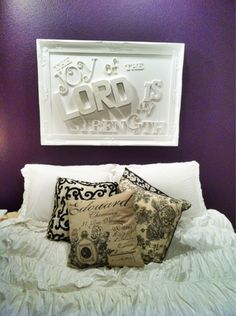 a bed with white sheets and pillows in front of a purple wall that has the word lord as seen on it