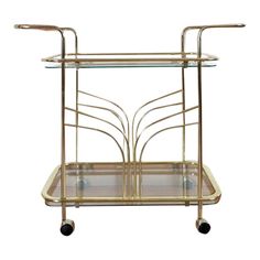 a brass serving cart with glass shelves and wheels on casteors, designed in the 1960s's