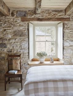 a bed sitting under a window next to a wooden table with a potted plant on it