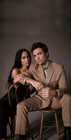 a man and woman sitting on top of a chair in front of a gray background