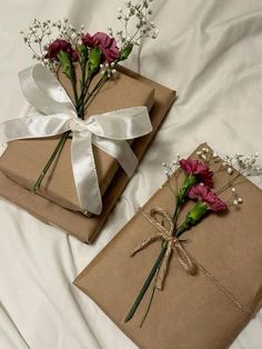 two wrapped gift boxes with flowers and ribbons tied around them on top of a bed