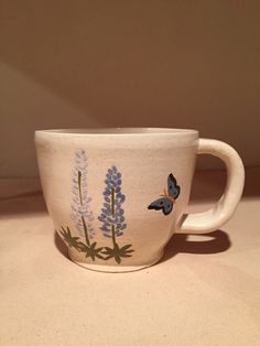 a white cup with blue flowers and butterflies on it sitting on top of a table