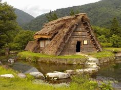 an old thatched house with a stream running through it