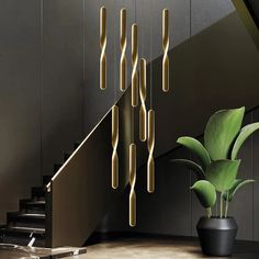 a plant in a black vase next to a stair case with gold rods hanging from it