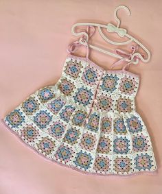 a crocheted dress hanging on a hanger with pink and blue flowers in it