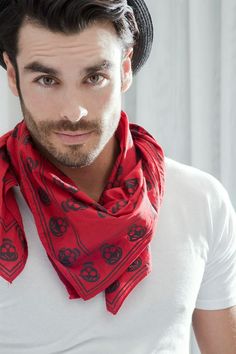 a man wearing a hat and red scarf with skulls on it is looking at the camera