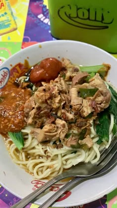 a white plate topped with pasta and meat next to a cup of coffee on a colorful table cloth