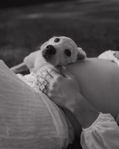 a black and white photo of a woman holding a dog on her lap while laying in the grass