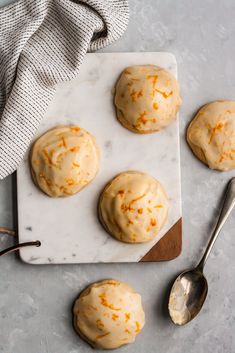 four cookies with orange icing on a cutting board next to a spoon and napkin