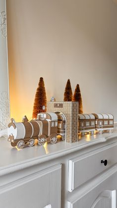 a toy train set on top of a white mantle next to a mirror and christmas trees