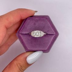 a woman's hand holding an engagement ring in a purple velvet box with a diamond center