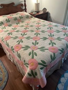 a bed with pink flowers on it in a bedroom next to a dresser and lamp