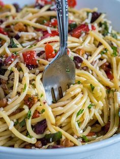 a white bowl filled with pasta and meat topped with parmesan cheese, olives, tomatoes and herbs