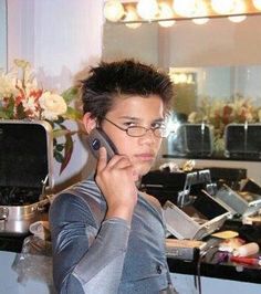 a young man wearing glasses is talking on his cell phone while standing in the kitchen