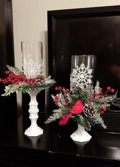 two white vases with red flowers and greenery sit on a table next to a mirror