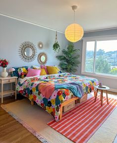 a bedroom with a large bed and colorful comforter on top of it, next to a window