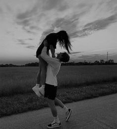 a man carrying a woman on his back while walking down the street at sunset in black and white