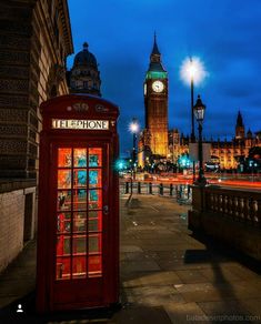 a red phone booth sitting on the side of a road next to a clock tower