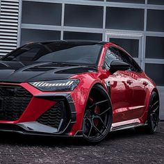 a red and black sports car parked in front of a garage door with its hood up