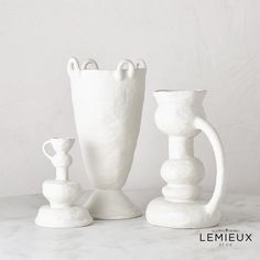 three white vases sitting next to each other on a marble counter top, with one holding a candle holder