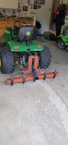 a green tractor with two large tires attached to it's front wheels in a garage