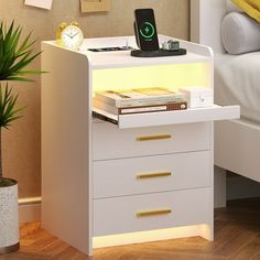 a white night stand with drawers and a phone on the top, next to a potted plant