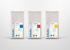 three bags of coffee sitting next to each other on a white surface with blue, yellow, and red labels