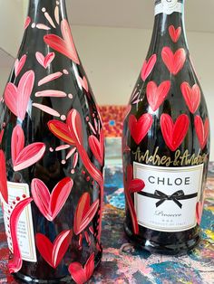 two wine bottles with hearts painted on them sitting on a colorful table cloth, one is black and the other is red