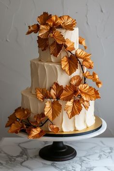 a three tiered cake with gold leaves on top