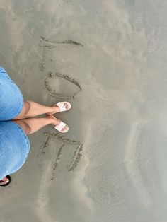 a woman standing in the sand with her feet in the water and writing on the sand