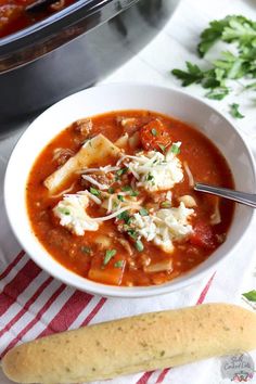 a bowl of soup with bread and parmesan cheese on the table next to it