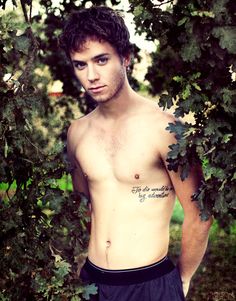 a shirtless young man standing in front of trees with his hands on his hips