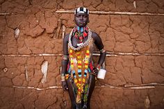 a woman standing in front of a stone wall wearing a colorful dress and headdress