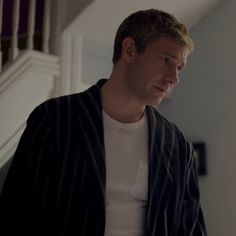 a man standing in front of a staircase talking to someone on his cell phone while wearing a white t - shirt and black blazer