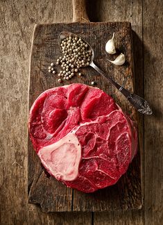 raw meat on a cutting board next to garlic and peppercorst with a spoon