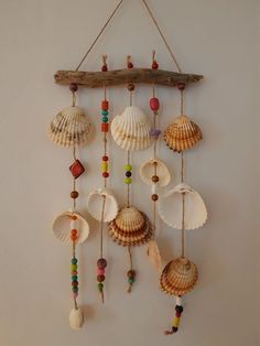 a wall hanging with seashells and beads attached to wood sticks on a white wall